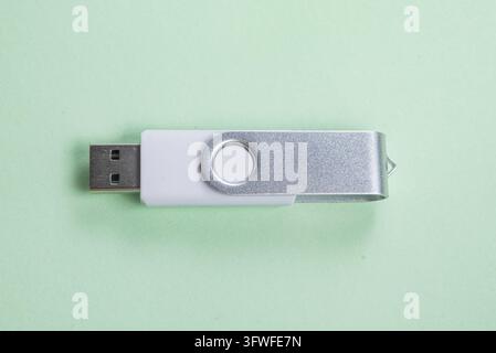 Una moderna chiavetta USB girevole bianca e argento è isolata su uno sfondo verde pastello, mostrando le sue capacità di archiviazione portatile e il design pulito Foto Stock