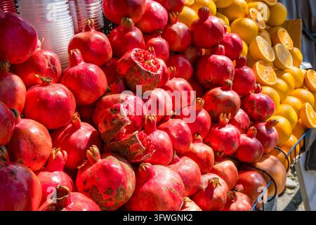 Bancarella di mercato colorata piena di melagrane rosse, inclusa frutta tagliata con semi visibili, accanto a arance intere e affettate alla luce solare intensa Foto Stock