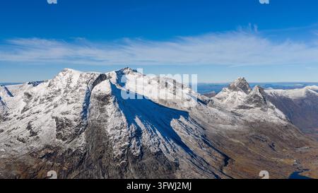Vista aerea delle cime innevate di Kongen e Alnestinden vicino a Trollstigen, che mostra il territorio montuoso impervio sotto un cielo blu limpido ad Andalsne Foto Stock
