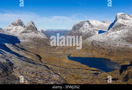 Vista aerea della tortuosa strada di montagna Trollstigen con i picchi Kongen e Alnestinden, un lago blu profondo e un terreno aspro e innevato ad Andalsnes Foto Stock