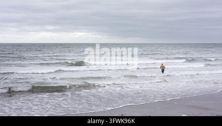 Un uomo solitario si avventura nel Mare del Nord a Cayton Bay, Yorkshire, Inghilterra, in una giornata autunnale. Foto Stock