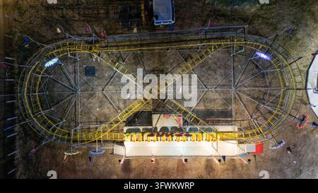 Veduta aerea di un roller coaster di un parco divertimenti con binari gialli e vagoni illuminati di notte in Serbia. Foto Stock