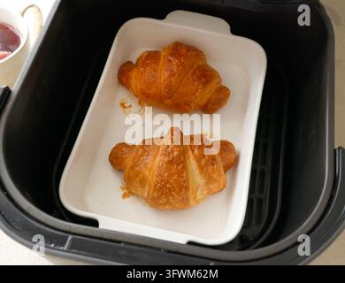 Croissant dorati appena sfornati in una teglia di ceramica dentro il cestello della friggitrice ad aria. Dessert per la colazione con pasta sfoglia fatta in casa apparecchio di cottura rapido moderno. Francese Foto Stock