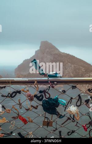 Una vista ravvicinata di una balaustra metallica ricoperta da vari elastici per capelli e un lucchetto, simboleggianti serrature d'amore, su uno sfondo sfocato di un paesaggio aspro Foto Stock