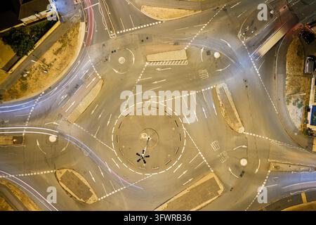 Di notte, le auto creano lunghe scie di luce attraverso un incrocio circolare, catturate da un punto elevato sopra il traffico urbano illuminato. Foto Stock