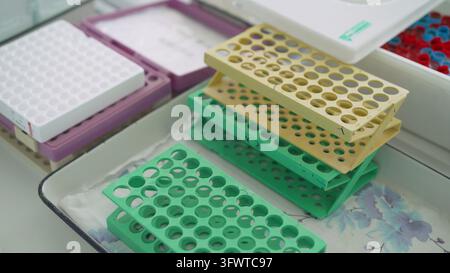 Primo piano di rastrelliere colorate per provette in plastica in un ambiente di laboratorio. Supporti verdi, gialli e bianchi per campioni scientifici sono disposti su un vassoio, pronti per Foto Stock