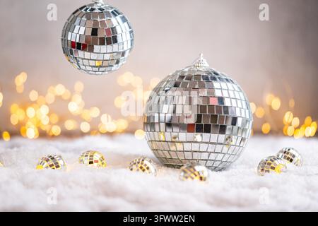 Uno sfondo natalizio con una grande palla da discoteca a specchio circondata da piccoli ornamenti riflettenti sulla neve, illuminata dolcemente da luci calde e tremolanti, ideale per disegni festivi per feste con spazio per il testo. Foto Stock