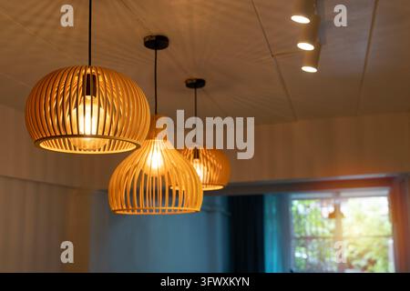 Tre lampade a sospensione in bambù intrecciato brillano caldamente sopra un interno moderno. Una luce dorata e soffusa crea un'atmosfera accogliente in un caffè o uno spazio da pranzo elegante. Backgr Foto Stock