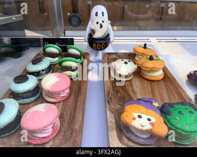 Vetrina da panetteria con tavole di legno e macarons colorati di Halloween a forma di fantasmi, zucche e streghe Foto Stock