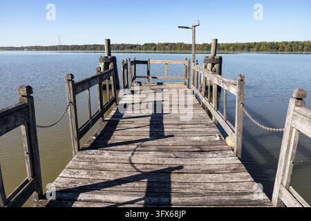 Un molo di pesca in legno stagionato si estende in acque calme vicino al campeggio di Whitten Park a Fulton, Mississippi, USA. Ringhiere in legno rustico, lunghe ombre Foto Stock