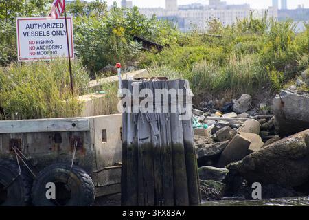 Brooklyn, NY – 17 set 2023: Cartello di avvertimento "Solo per imbarcazioni autorizzate" e bandiera degli Stati Uniti sopra un palo di legno, paraurti in gomma e rocce sulla riva di Red Hook. Foto Stock