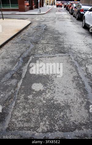 Manhattan, New York City, USA – 24 dicembre 2023: Vista ad alta angolazione di una strada asfaltata crepata e rattoppata con auto parcheggiate a Lower Manhattan. Foto Stock
