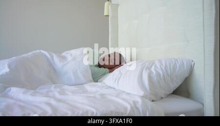 Donna di mezza età che dorme in camera da letto sotto un piumino bianco con una maglia verde chiaro, con testiera e lampada. Addormentata, serena, minimalista, diffusa, smorzata, biancheria da letto Foto Stock