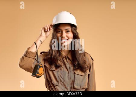 Giovane architetta sorridente si aggiusta il casco in uno studio minimalista caldo durante una giornata lavorativa. Foto Stock