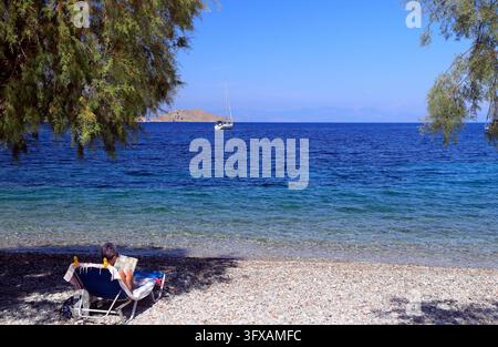 Donna su una sedia da letto che legge libri, Livadia Beach, Tilos, Isole Dodecaneso, Egeo Meridionale, Grecia. Foto Stock