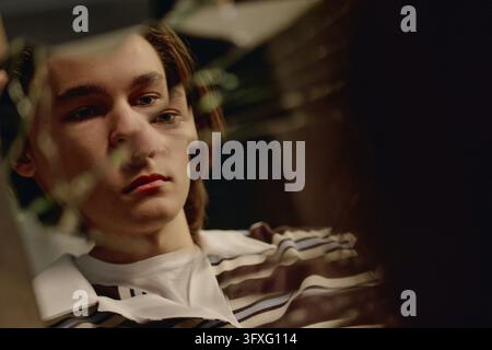 Adolescente maschio depresso che guarda il suo riflesso in uno specchio rotto Foto Stock