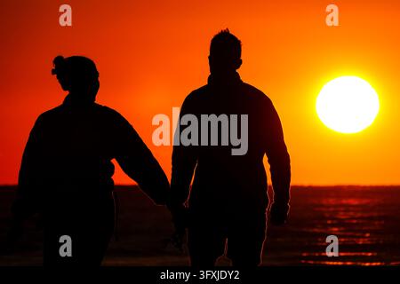 Isle of Palms, Stati Uniti. 23 ottobre 2026. Una coppia cammina insieme lungo la spiaggia silouettata dal sole che sorge sull'Oceano Atlantico, 23 ottobre 2026 a Isle of Palms, South Carolina. Credit: Richard Ellis/Richard Ellis/Alamy Live News Foto Stock