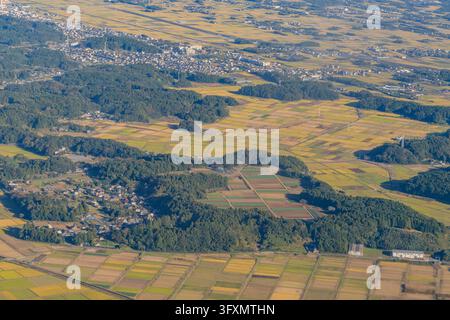 Veduta aerea ad alta angolazione di un paesaggio rurale con campi di riso a chiazze, colline boscose e una città a Chiba, Giappone. Foto Stock
