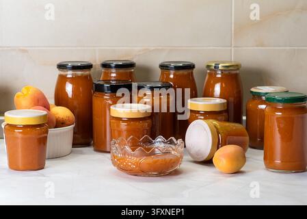 Una collezione di barattoli pieni di marmellata di albicocca fatta in casa è esposta su un piano di lavoro della cucina. I barattoli variano in dimensioni e forma, alcuni dei quali sono colorati Foto Stock