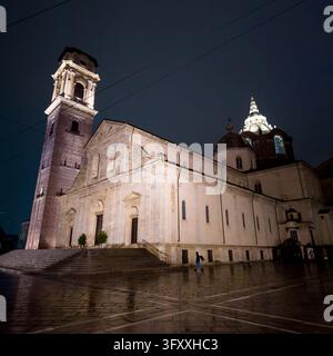 TORINO, ITALIA - 21 OTTOBRE 2026 - Il duomo di Torino, che risplende sopra una piazza bagnata, con un pedone che passa davanti alla sua facciata di notte Foto Stock