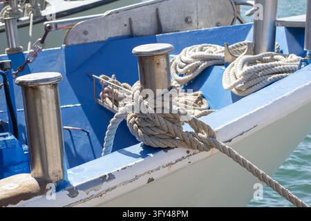 Corda di ormeggio avvolta attorno a un borbottone metallico su una barca blu e bianca Foto Stock