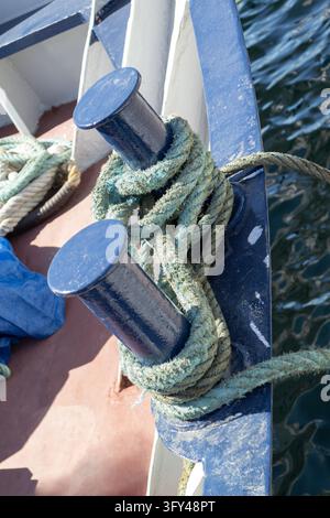 Corda di ormeggio consumata avvolta intorno a bittelle blu su una barca Foto Stock