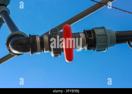 Un tubo di plastica nero con una maniglia della valvola rossa impostata in posizione chiusa su un cielo blu chiaro. Foto Stock