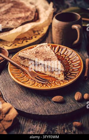 Fetta di torta a strati di mandorle e cannella con glassa cremosa e spolverata di cacao su un piatto di ceramica Foto Stock