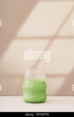 Bevanda matcha in tazza di vetro con cannuccia di vetro su sfondo beige. Luce e ombra. Concetto minimalista di tè verde matcha sano. Idea creativa e trendy per una bevanda Foto Stock