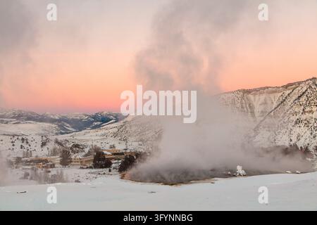 Un tramonto vivace proietta una luce calda su Palette Spring, una prominente terrazza di travertino situata nell'area delle Mammoth Hot Springs del Parco Nazionale di Yellowstone, Wyoming, USA. Le acque termali ricche di carbonato di calcio disciolto si riversano lungo terrazze calcaree a gradini, nutrendo tappeti colorati di microorganismi termofili. Una passerella per i visitatori attraversa il paesaggio innevato in inverno, consentendo un accesso sicuro per osservare il sistema idrotermale attivo, le bocche di vapore e le delicate formazioni minerali create da un An Versione ottimizzata di un'immagine del US National Park Service. Credit: NPS Foto Stock