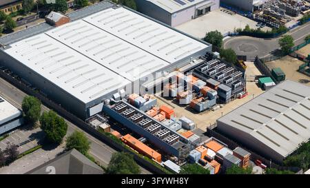 Vista aerea di un complesso di data center con apparecchiature di alimentazione di emergenza, unità di raffreddamento e container di servizio accanto a edifici industriali che supportano la Foto Stock