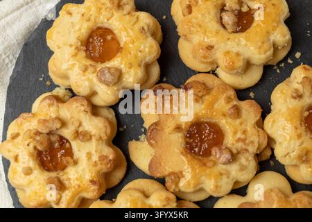 Vista dall'alto di biscotti shortbread dorati a forma di fiore, appena sfornati, con glassa d'uovo lucida, ripieni di marmellata di albicocca e ricoperti di noci tritate Foto Stock