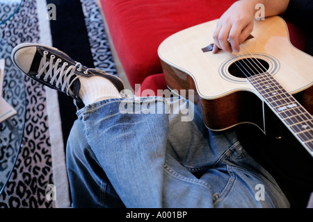 Giovane maschio suonando una chitarra acustica a casa seduto sul suo lettino. Foto Stock