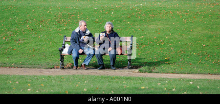 Accoppiare due persone seduta su una panchina di mangiare in Buxton Inghilterra del Nord UK UE parco Prato verde età di riposo giornata estiva colore orizzontale Foto Stock