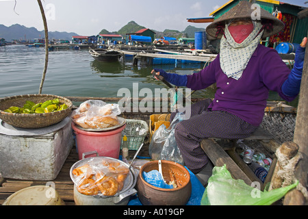 Donna vendita ciambelle di pane frutta e bevande righe il suo negozio intorno a floating villaggio di pescatori Cat Ba Town Bay a nord-est del Vietnam Foto Stock