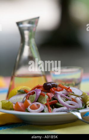 Una insalata greca piastra caraffa di Retsina vino bianco e vetro colorato sulla tovaglia. Colpo di luce diurna. Focus sul piatto di insalata Foto Stock