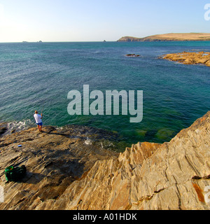 Fisherman su rocce esposte a bassa marea a Treyarnon Bay North Cornwall con testa Trevose all'orizzonte Foto Stock