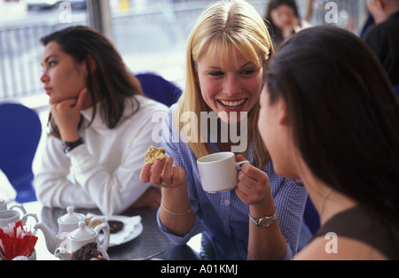 Le giovani donne a chattare in un caffè mentre un amico sembra triste e lasciato fuori Foto Stock