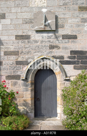 Ritratto che mostra la porta in legno sul lato della costruzione in pietra con sun dial sopra e le rose attorno al lato sinistro Foto Stock