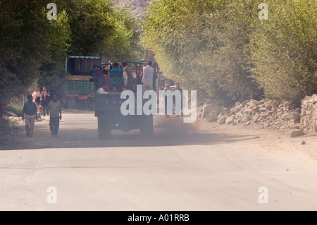 Camion diesel che produce smog nero in aria a basso contenuto di ossigeno su una strada a Ladakh, India. La gente cammina lungo il polveroso sentiero di montagna fiancheggiato da alberi. Foto Stock