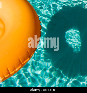 Arancione anello gonfiabile galleggianti in un blu piscina getta un' ombra Foto Stock