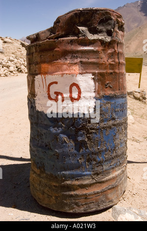 Vecchio barile di benzina con cartello GO, tamburo metallico arrugginito e intempestivo su una strada desertica con montagne sullo sfondo. Foto Stock