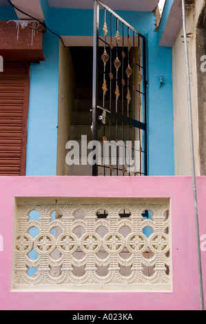 Ingresso casa rosso e blu nello stato indiano dell'Himachal Pradesh, caratterizzato da una parete decorativa rosa e da un cancello in metallo nero che conduce alle scale. Foto Stock