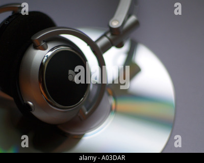 Cuffie argento recante sulla cima di un lucido compact disc nel fuoco poco profonde e molto tenue illuminazione. Foto Stock