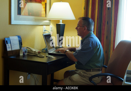 Imprenditore usando un computer portatile su una scrivania in una stanza di un hotel Foto Stock