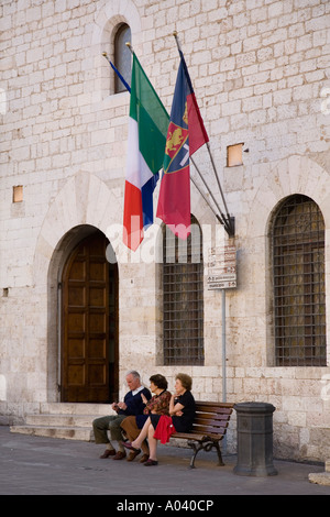 Tre persone sedersi sulla panchina sulla Piazza del Comune di fronte al Palazzo Comunale in hilltown umbra di Assisi Italia PG Foto Stock