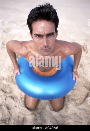Ritratto di un giovane uomo che indossa un gonfiabile blu anello in gomma intorno alla vita Inginocchiati sulla spiaggia Foto Stock
