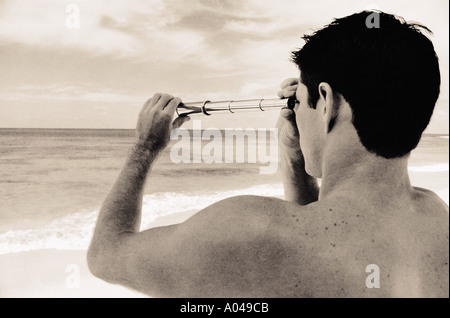 Giovane uomo in piedi sulla spiaggia affacciata sul mare con un telescopio Foto Stock