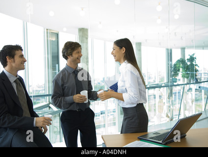 Tre impiegati in piedi con tazze di caffè, parlando Foto Stock