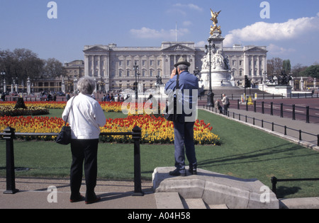 Cielo blu giorno soleggiato per coppia di turisti che scattano foto dei tulipani primaverili fuori Buckingham Palace e Victoria Memorial The Mall London England UK Foto Stock